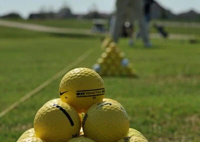 A closeup of yellow golf balls stacked at the driving range with golfers distant in the background.