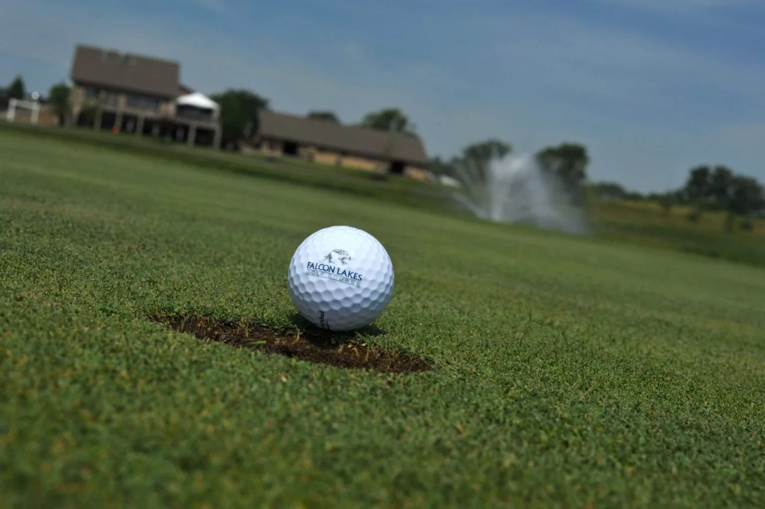 A golf ball bearing the Falcon Lakes logo is resting on the green.
