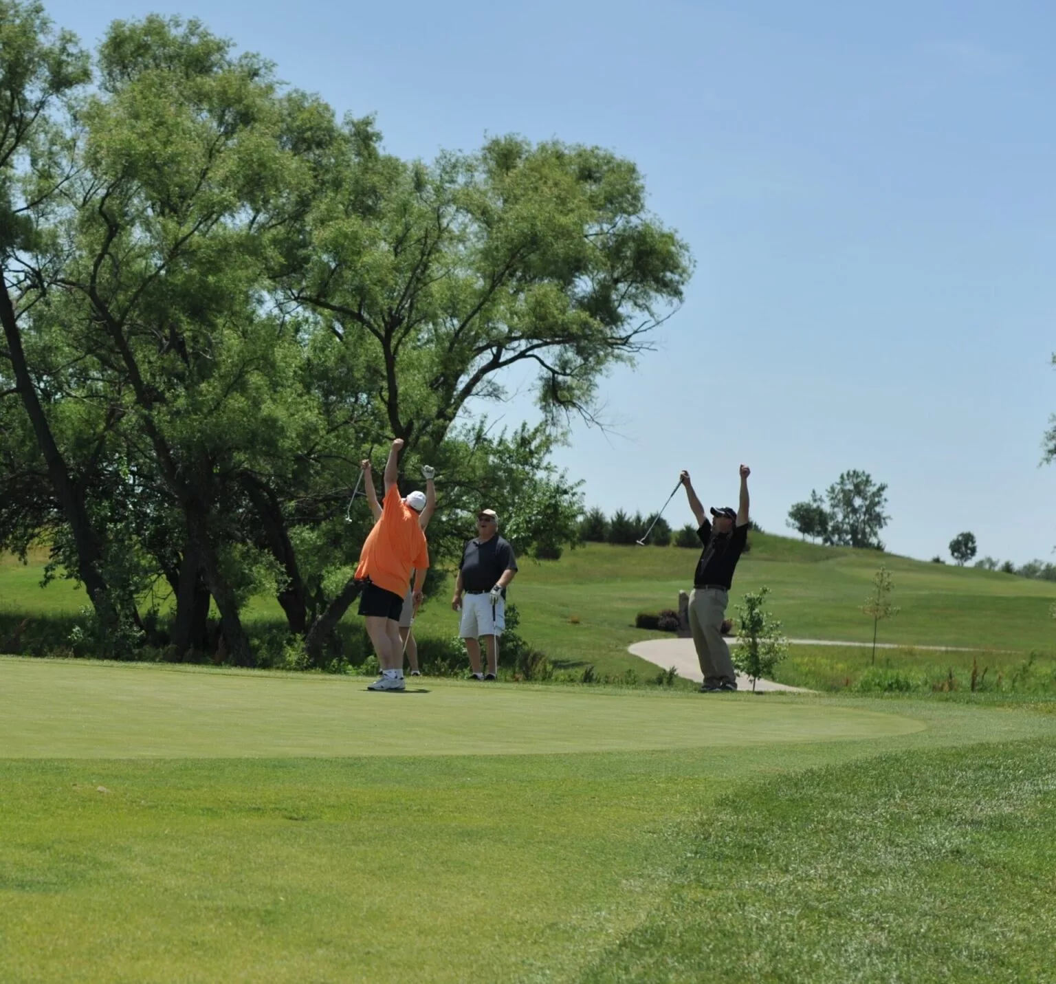 A group of golfers are celebrating on the green with clubs in hand.