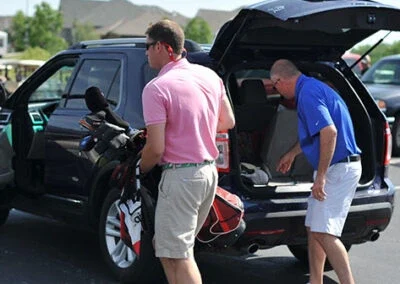 Golfers are unloading their gear from the back of an SUV.
