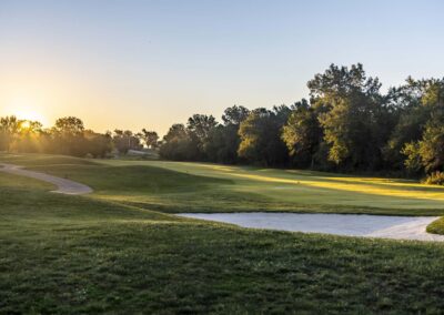 Photo of Falcon Lakes Golf Course showing bunker, cart path, and trees during a sunrise.